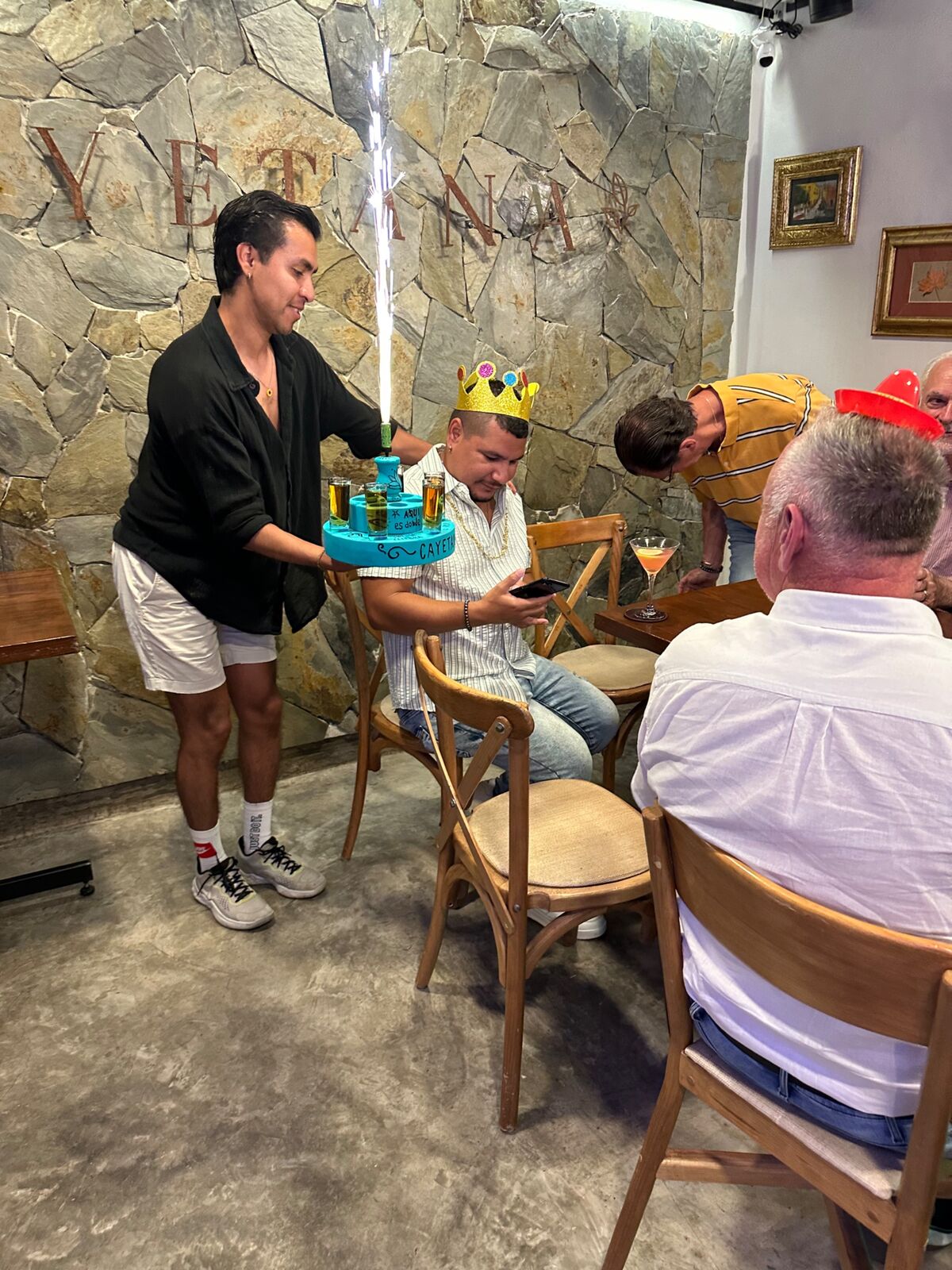 Mesero llevando una torre de shots con bengala a un cumpleañero con corona